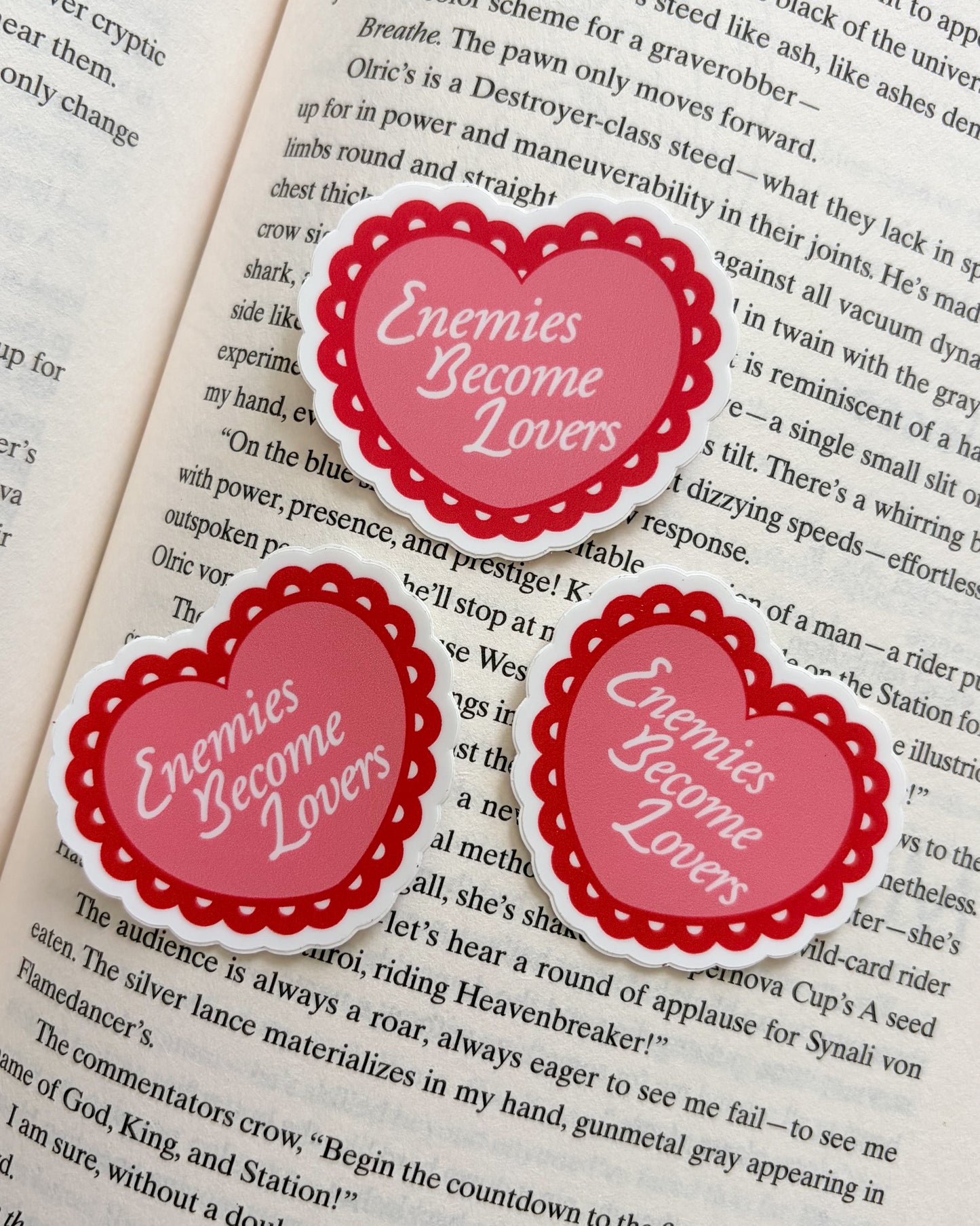 Heart-shaped stickers with 'Enemies Become Lovers' text on a book page