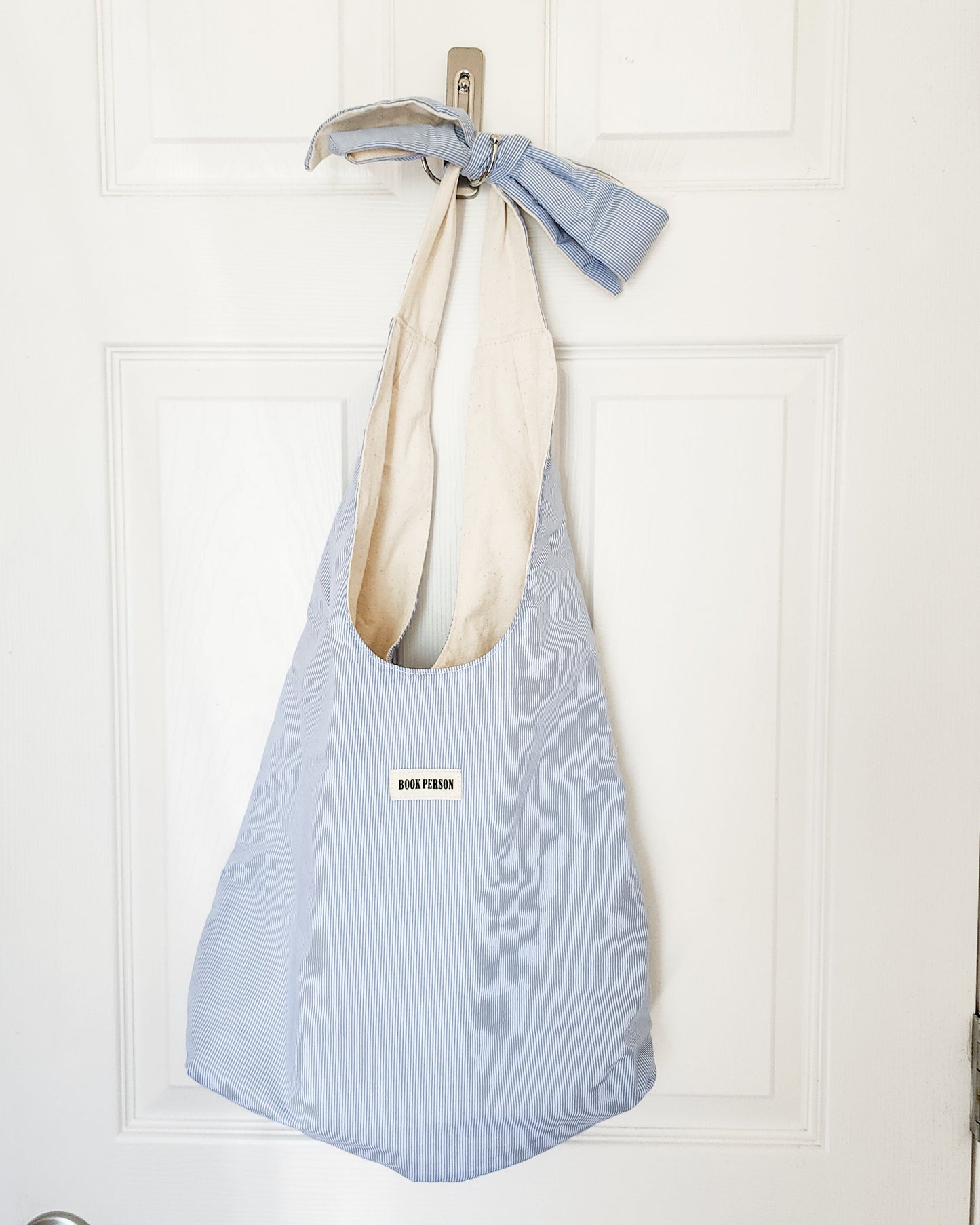 Blue striped tote bag with 'Book Person' patch and bow handle hanging on white door
