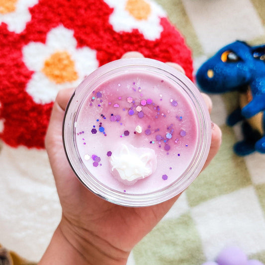 Pink glittery slime with white cloud charm, held over floral rug and blue dragon toy
