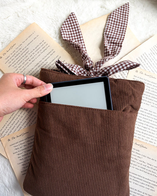Brown corduroy e-reader sleeve with bunny ears, hand inserting device, vintage book pages background