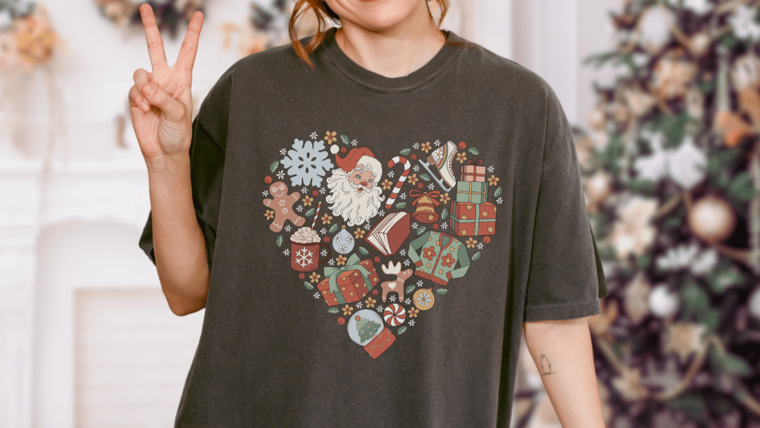 Black t-shirt with heart-shaped Christmas print featuring Santa, books, gifts, and festive icons.