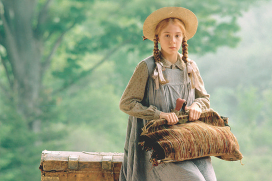 Young girl in vintage dress and straw hat holding a pillow, surrounded by greenery