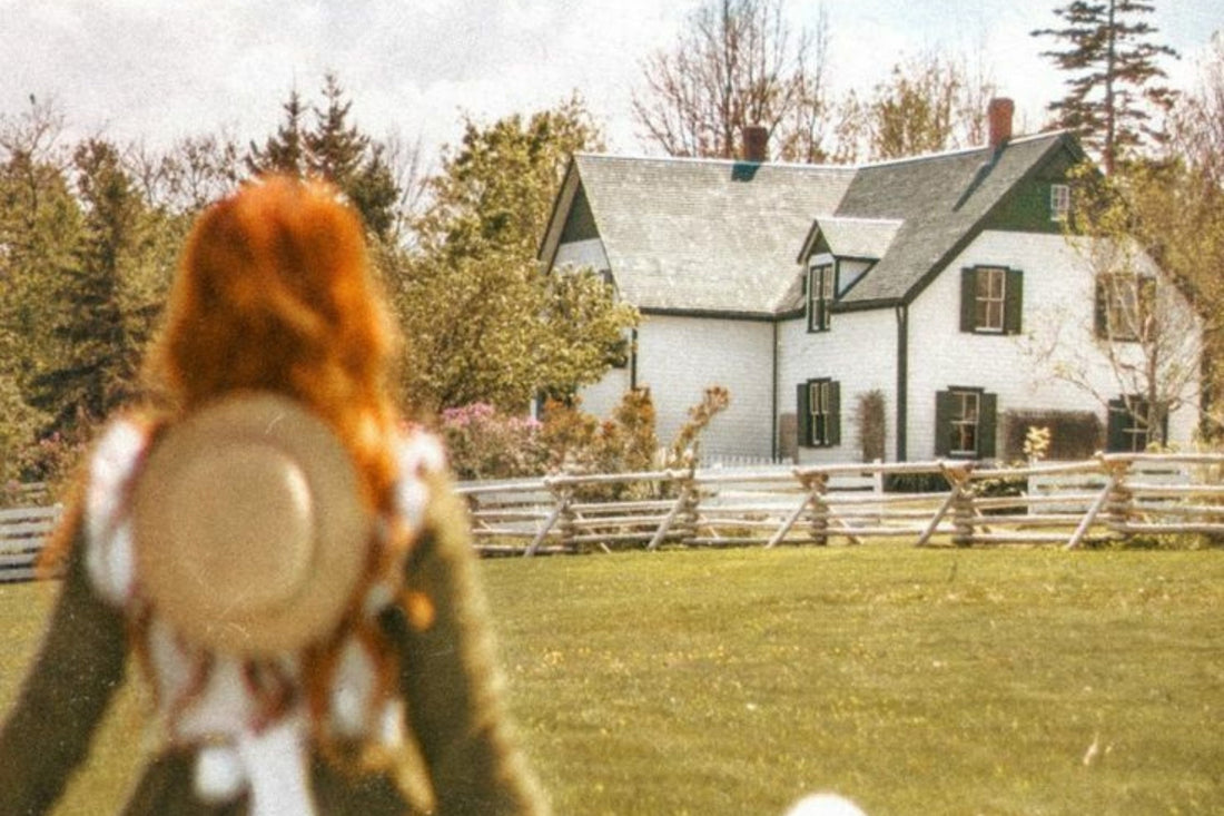 Red-haired woman with straw hat faces white farmhouse with green shutters, surrounded by trees and fence.