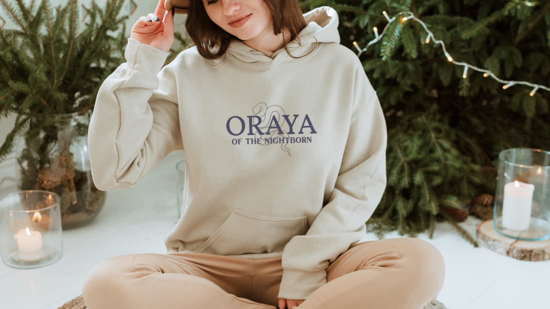Woman wearing Oraya of the Nightborn hoodie, sitting near Christmas tree with candles