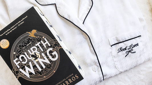 White 'Book Lover' pajamas with black trim beside 'Fourth Wing' book, perfect for bookish fans.