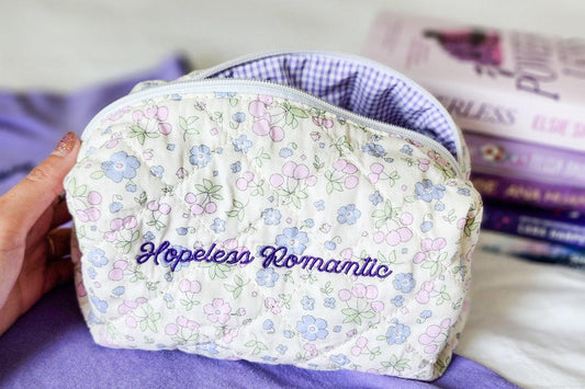 Floral quilted pouch with 'Hopeless Romantic' embroidery, books in background, purple tones