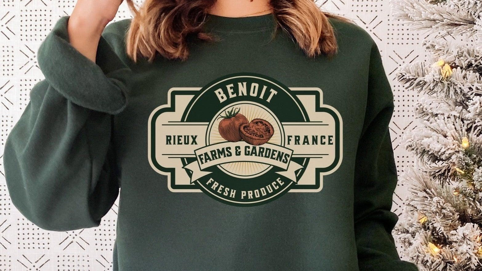 Person wearing dark green sweatshirt with Benoit Farms & Gardens tomato graphic, next to snowy Christmas tree.