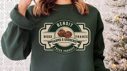 Person wearing dark green sweatshirt with Benoit Farms & Gardens tomato graphic, next to snowy Christmas tree.
