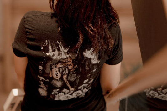 Person wearing black t-shirt with fantasy book-inspired artwork and holding a book
