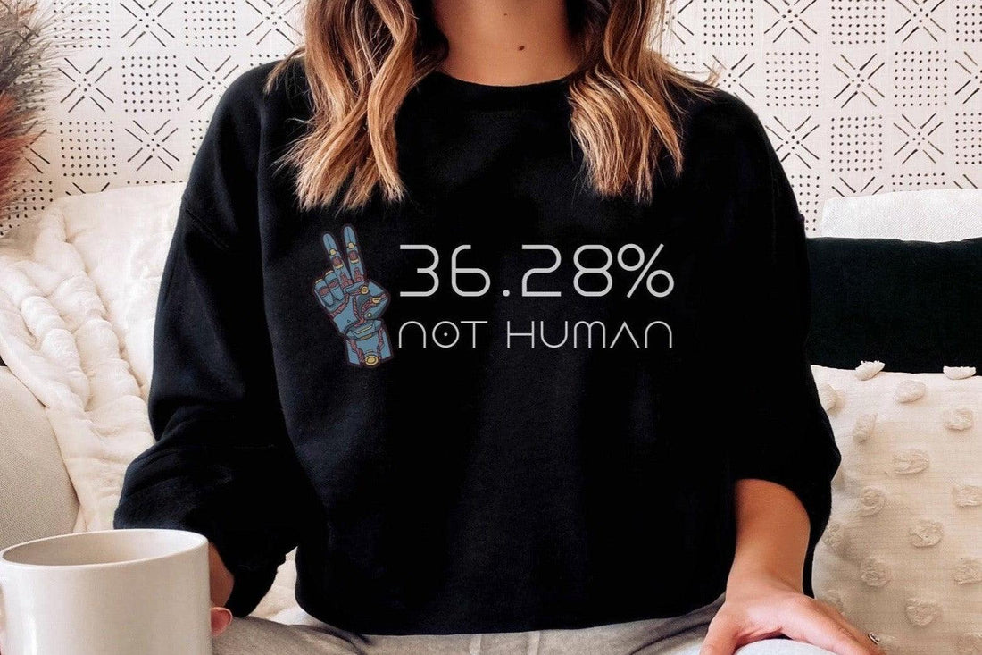 Person wearing black sweatshirt with '36.28% not human' robot hand graphic, holding coffee mug.