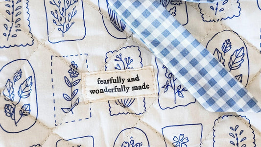 Quilted fabric with blue floral patterns and 'fearfully and wonderfully made' tag, bookish merch design