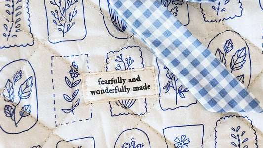 Quilted fabric with blue floral patterns and 'fearfully and wonderfully made' tag, bookish merch design