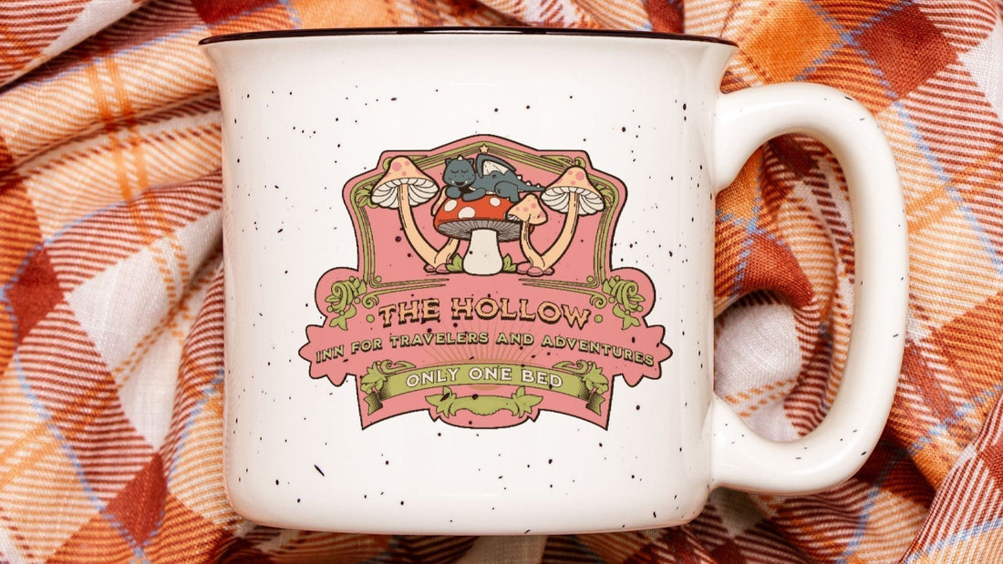 White ceramic camp mug with whimsical mushroom and cat design, bookish quote, on plaid fabric.