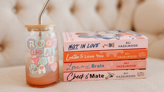 Stack of colorful Ali Hazelwood books and pastel glass tumbler with 'Read What You Want' text
