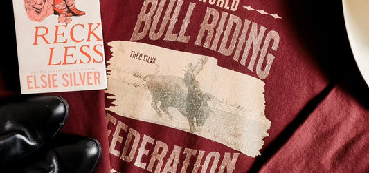 Reckless book by Elsie Silver on maroon shirt with rodeo bull riding design and black boots