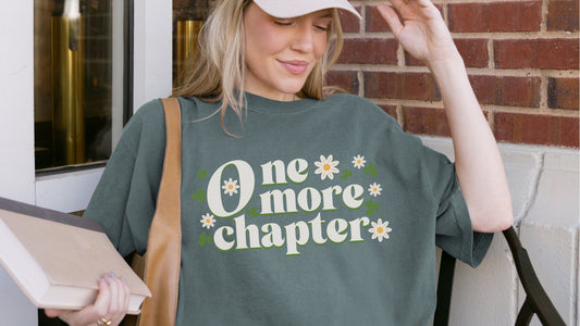 One more chapter t-shirt with daisies and clovers, worn by woman holding book