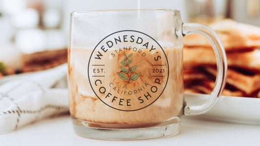 Glass coffee mug with swirling iced coffee and Wednesday's Coffee Shop logo, waffles in background