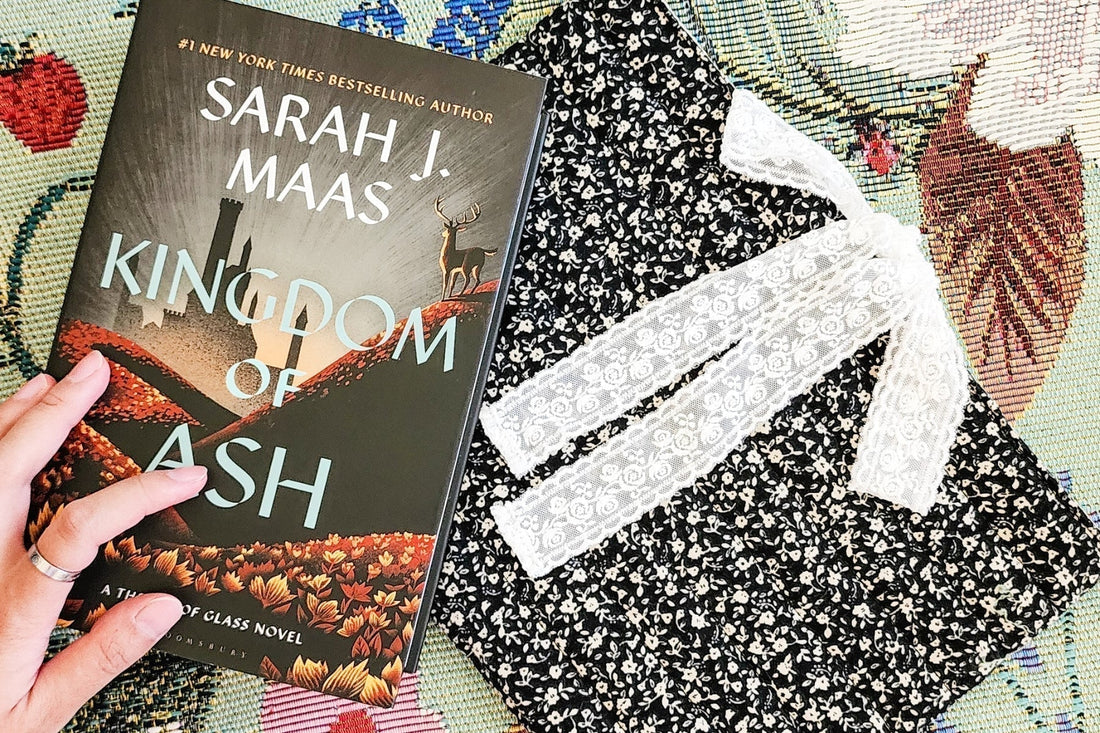 Kingdom of Ash book with a floral pouch and lace bow on a patterned fabric surface