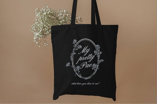 Black bookish tote bag with floral design and white script, filled with baby's breath flowers
