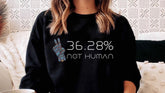 Woman in cozy room wearing black sweatshirt with '36.28% not human' text and robot hand graphic