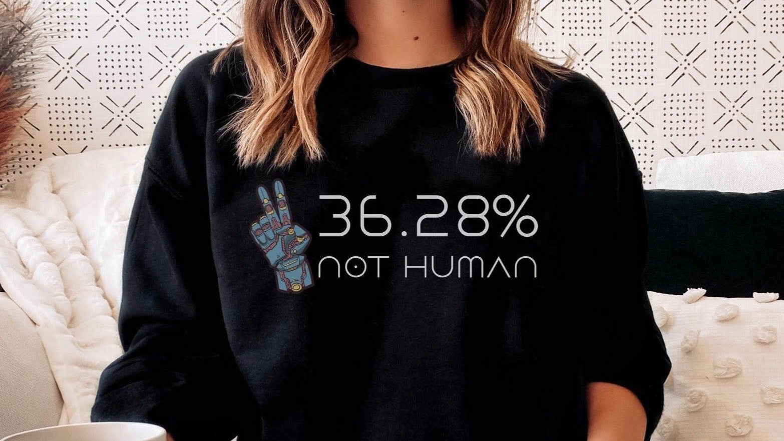 Woman in cozy room wearing black sweatshirt with '36.28% not human' text and robot hand graphic