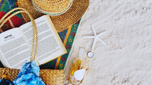 Open book, straw hat, starfish, and drink on sand for beach reading scene
