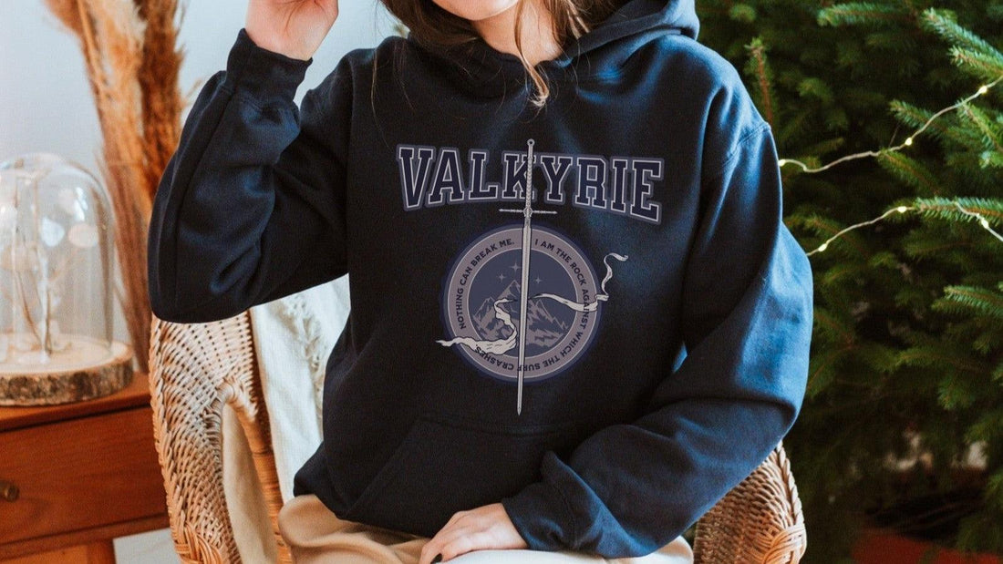 Person wearing a black Valkyrie hoodie with sword and mountain graphic, cozy indoor setting