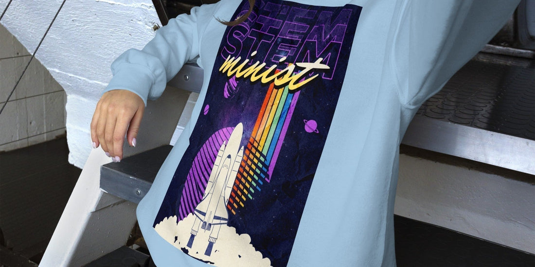 Light blue sweatshirt with a colorful STEM feminist rocket and space graphic design