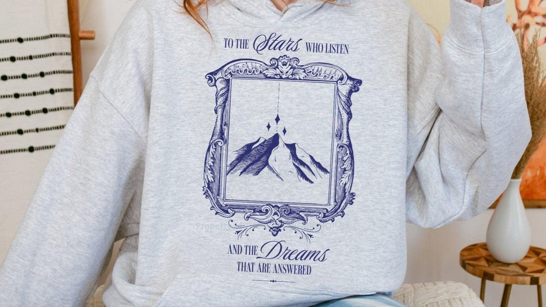 Light gray hoodie with bookish mountain and stars illustration, literary quote on front