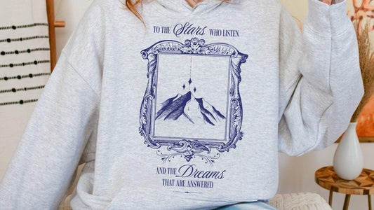 Light gray hoodie with bookish mountain and stars illustration, literary quote on front