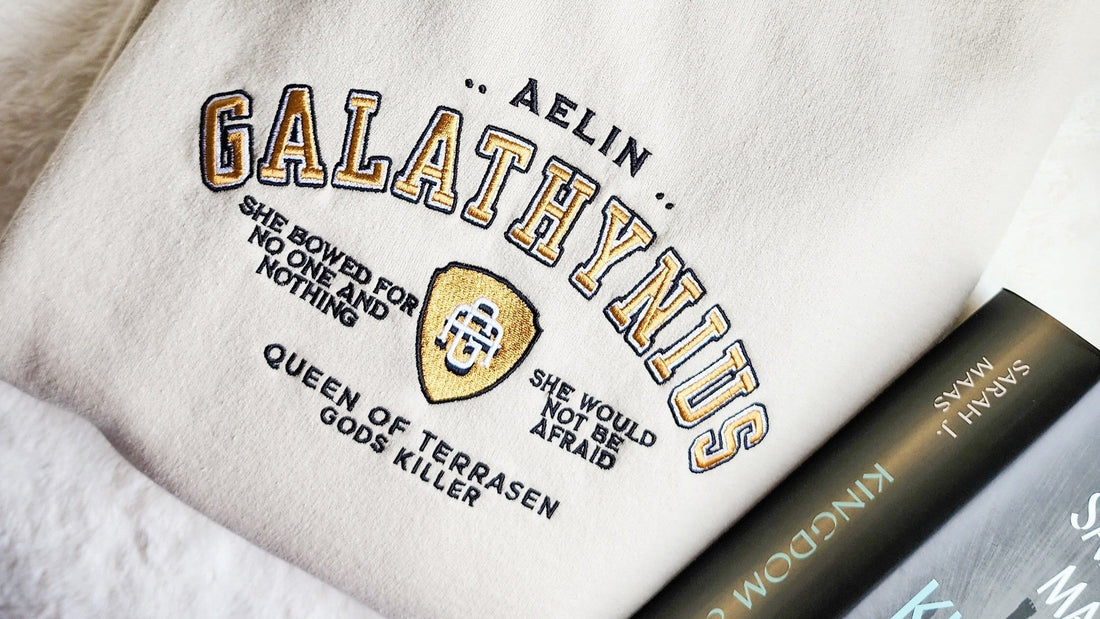 Embroidered sweatshirt with 'Aelin Galathynius' design, Throne of Glass book by Sarah J. Maas nearby.