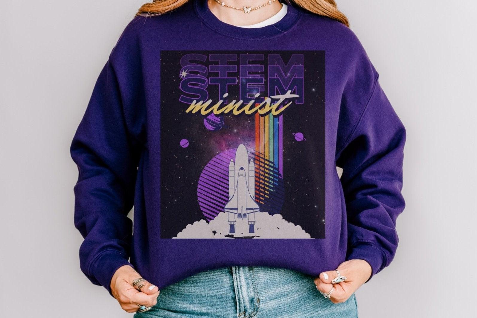 Purple STEMinist sweatshirt with rocket ship and rainbow, space-themed design