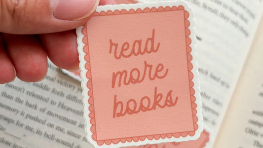 Pink read more books sticker with scalloped border held above an open book