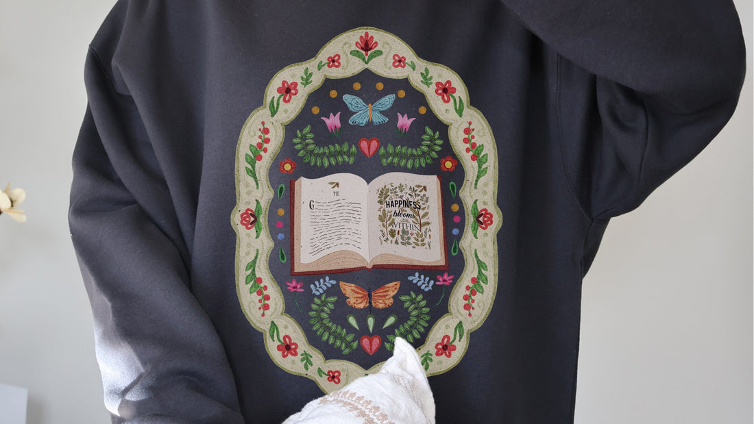 Bookish hoodie with floral design, butterflies, and 'Happiness blooms within' quote for book lovers.