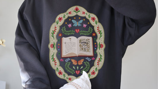 Bookish hoodie with floral design, butterflies, and 'Happiness blooms within' quote for book lovers.