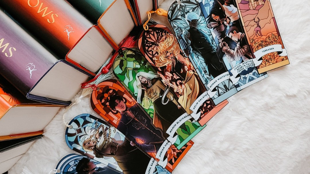 Colorful fantasy book-inspired bookmarks with character art beside stacked hardcover books