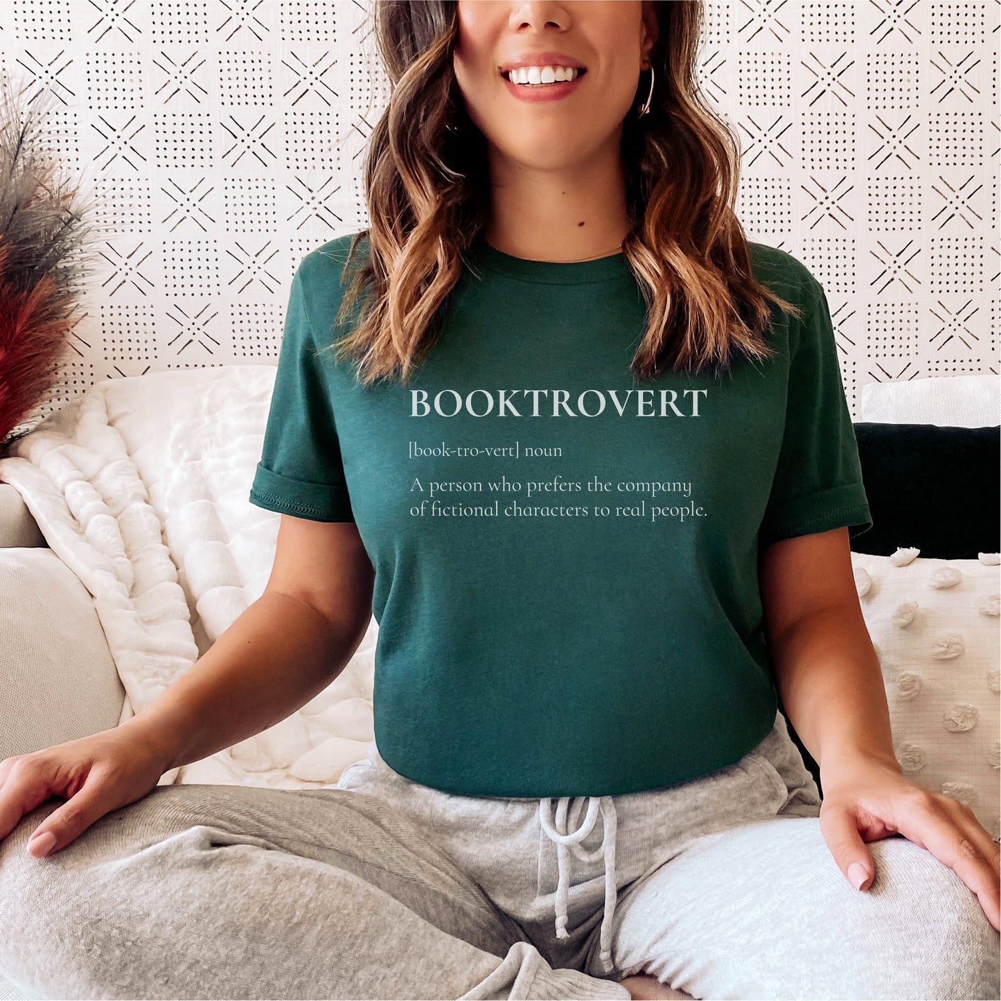 Woman wearing green Booktrovert t-shirt with bookish slogan sitting on couch