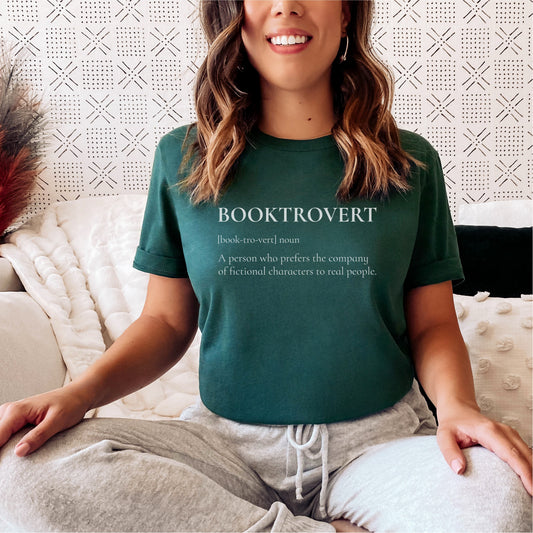 Woman wearing green Booktrovert t-shirt with bookish slogan sitting on couch
