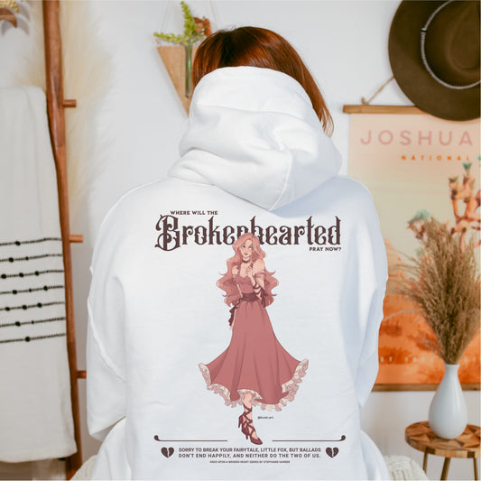 White hoodie with "Brokenhearted" fantasy art and text, bookish merchandise, worn indoors.