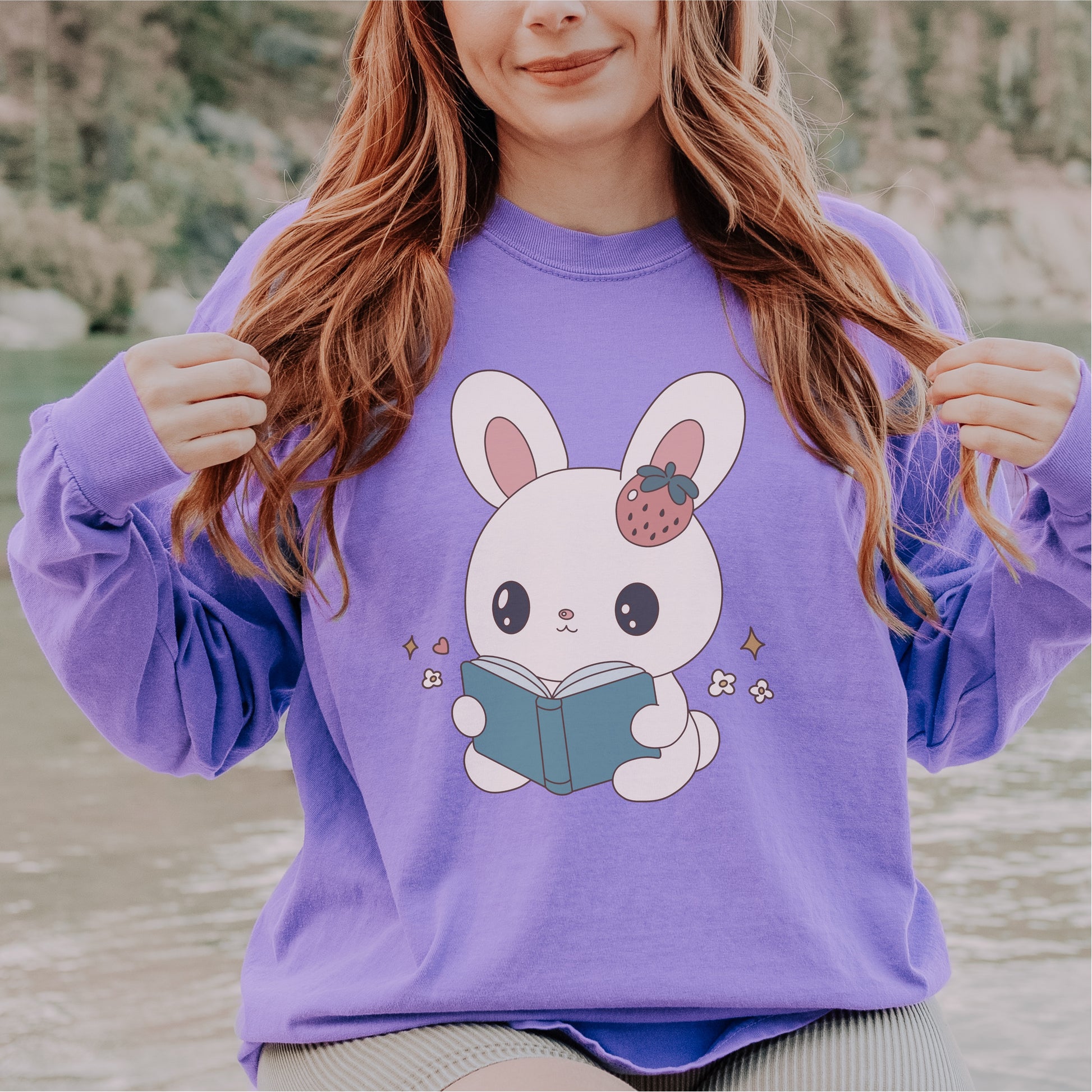 Purple long sleeve tee with cute bunny reading a book graphic, outdoors setting