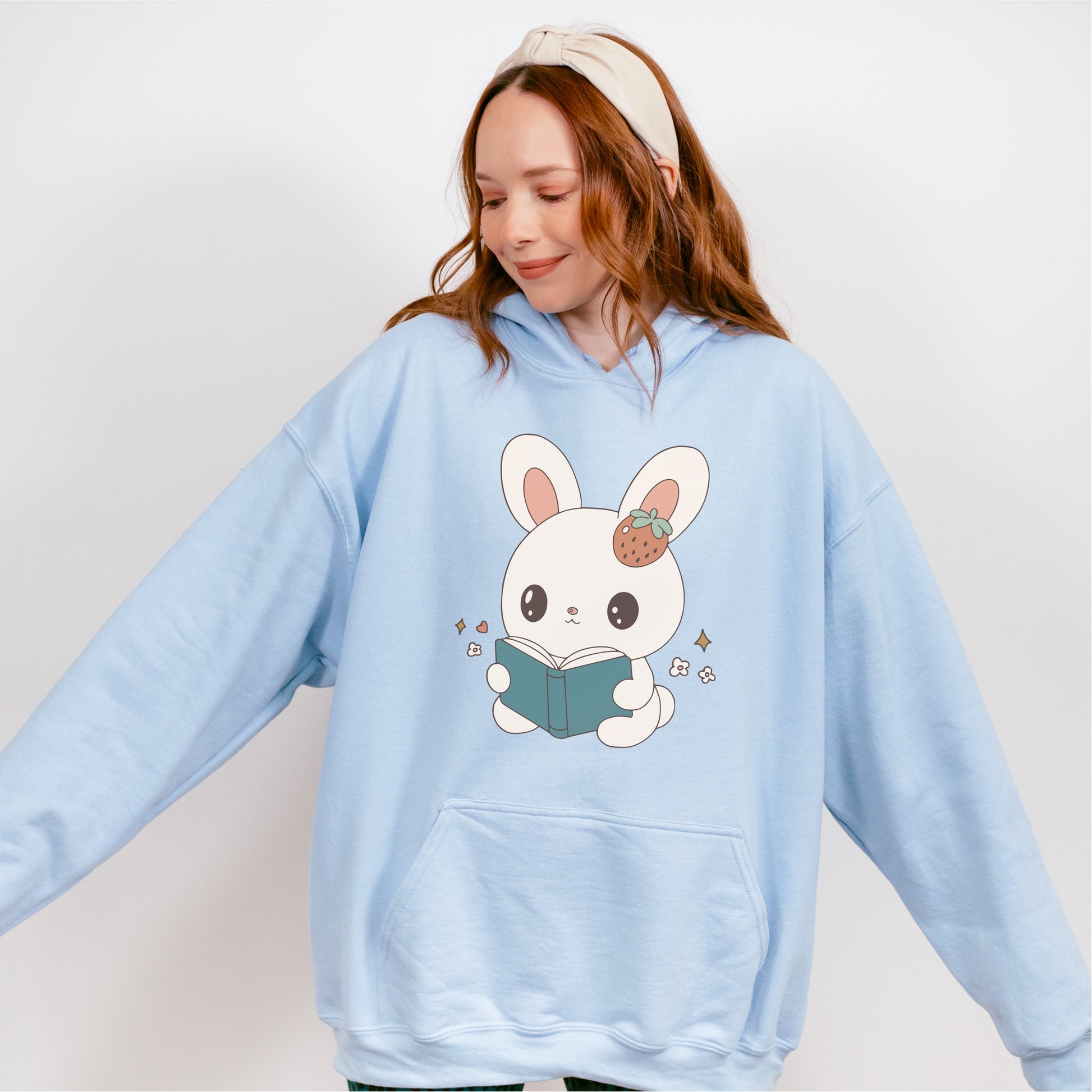 Light blue hoodie with cute bunny holding a book graphic, worn by woman with headband