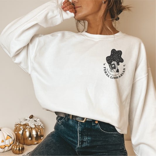 Woman wearing white Feral Librarian sweatshirt with bookish graphic, styled with jeans, pumpkins decor