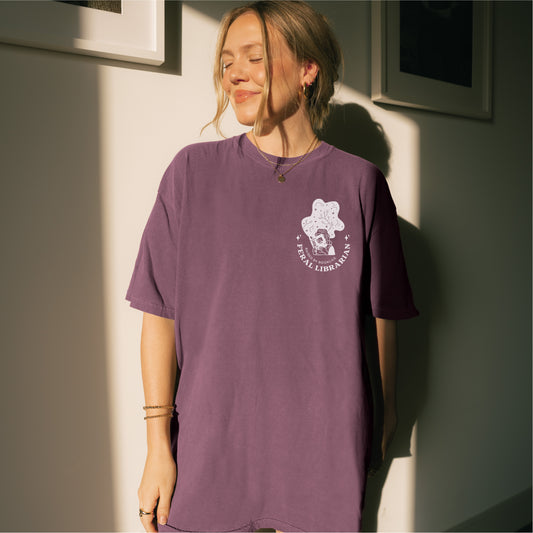 Woman wearing purple Feral Librarian t-shirt with graphic and text on chest, bookish apparel