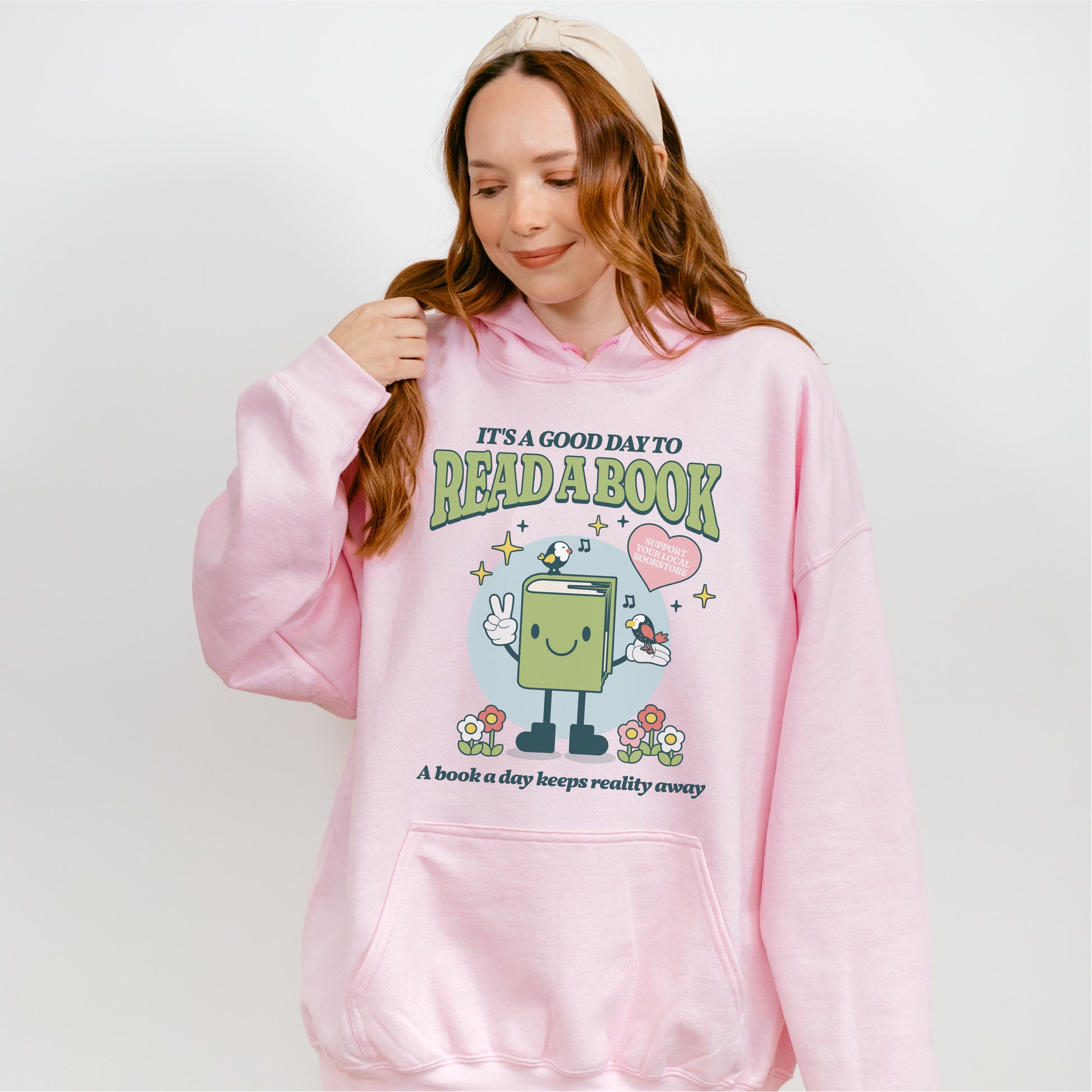 Woman wearing pink hoodie with cartoon book design and 'It's a good day to read a book' text.