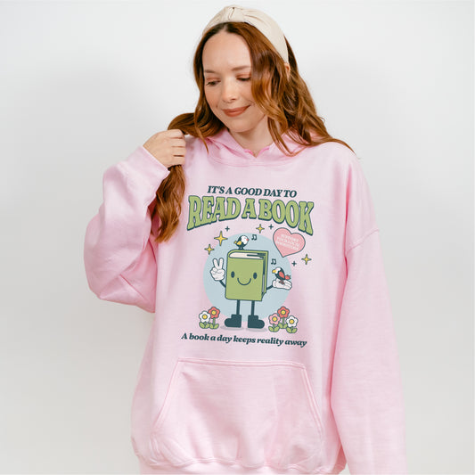 Woman wearing pink hoodie with cartoon book design and 'It's a good day to read a book' text.
