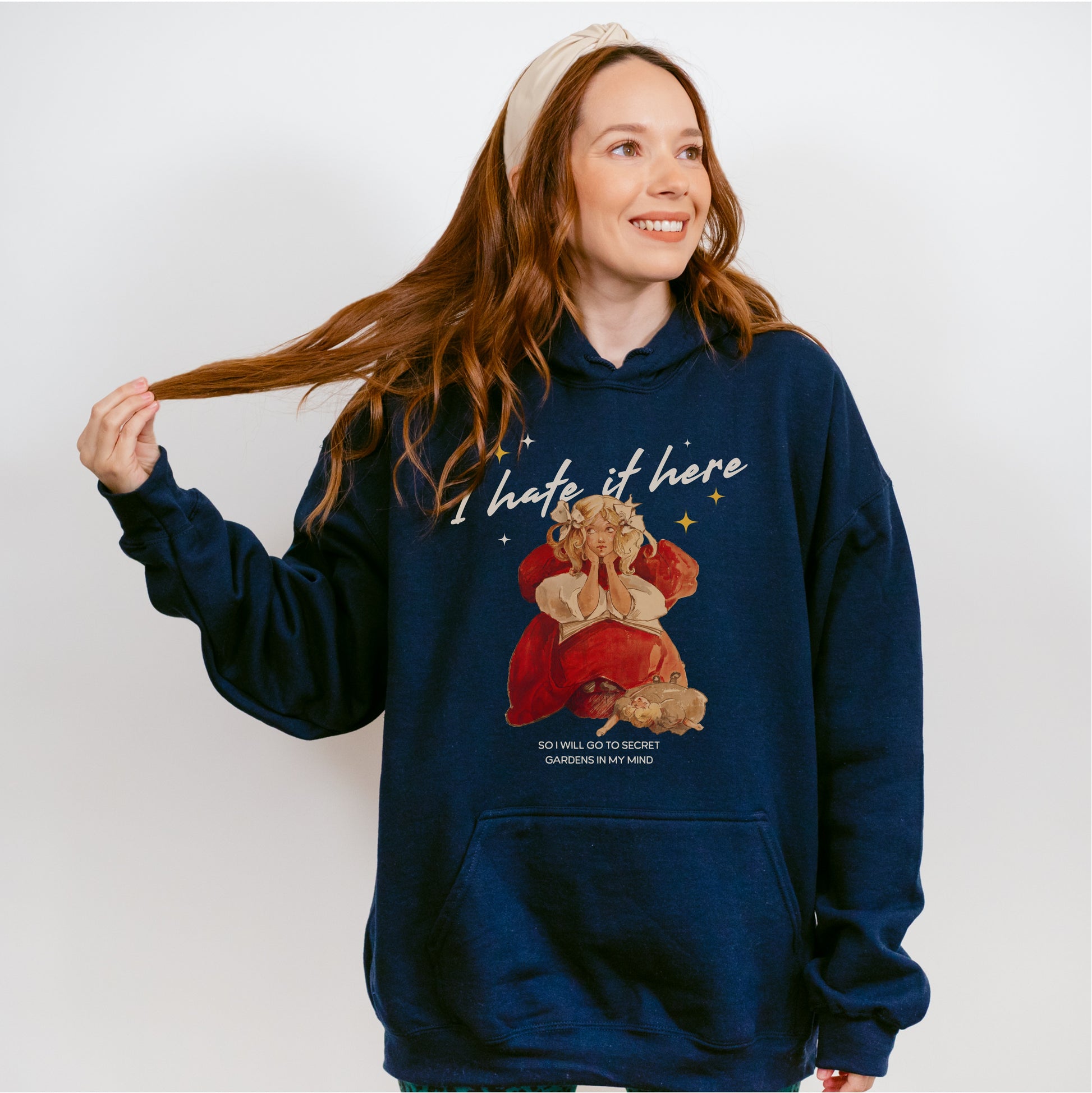 Woman wearing navy blue hoodie with 'I hate it here' text and illustrated bookish character