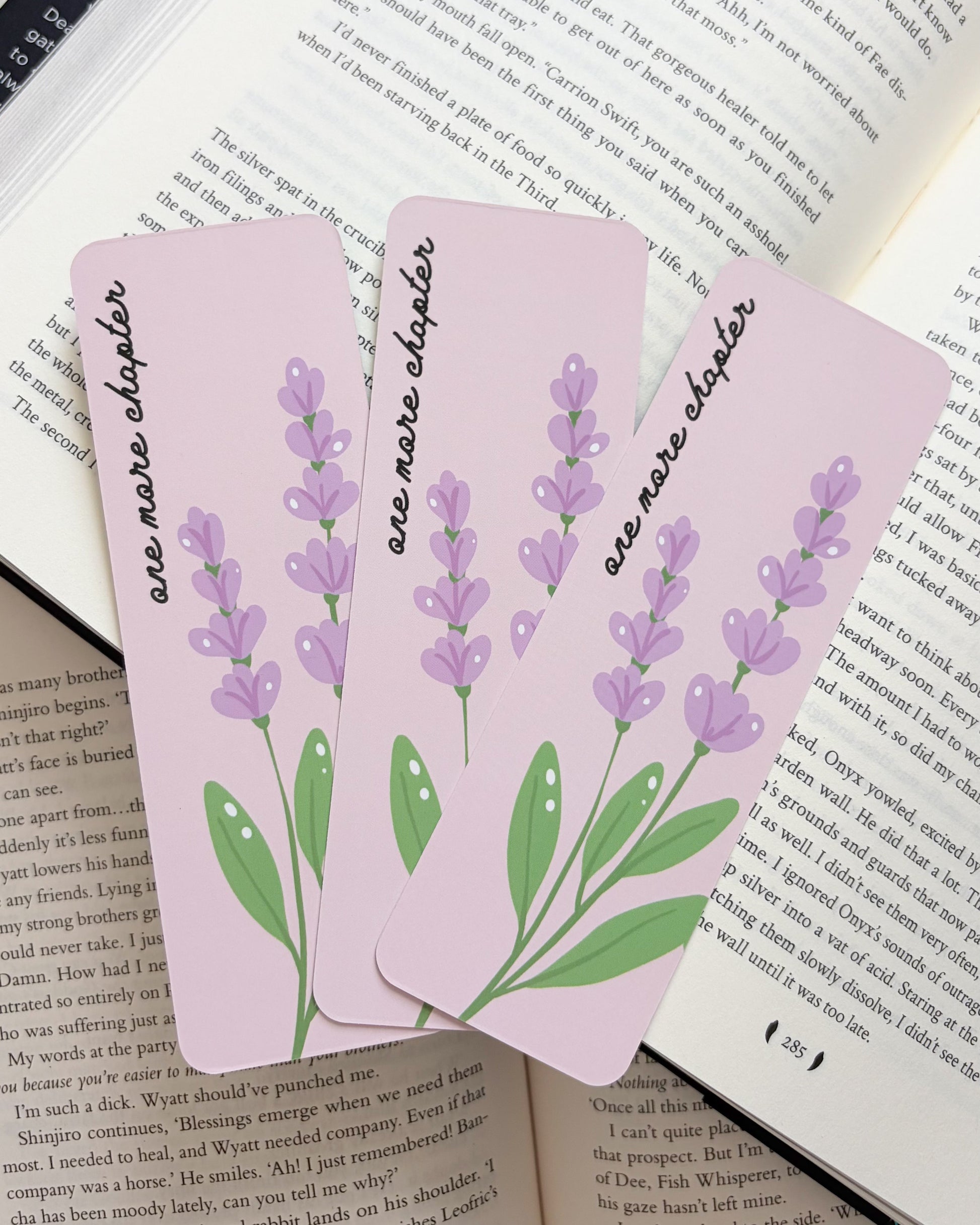 Three pink bookmarks with lavender designs on an open book.