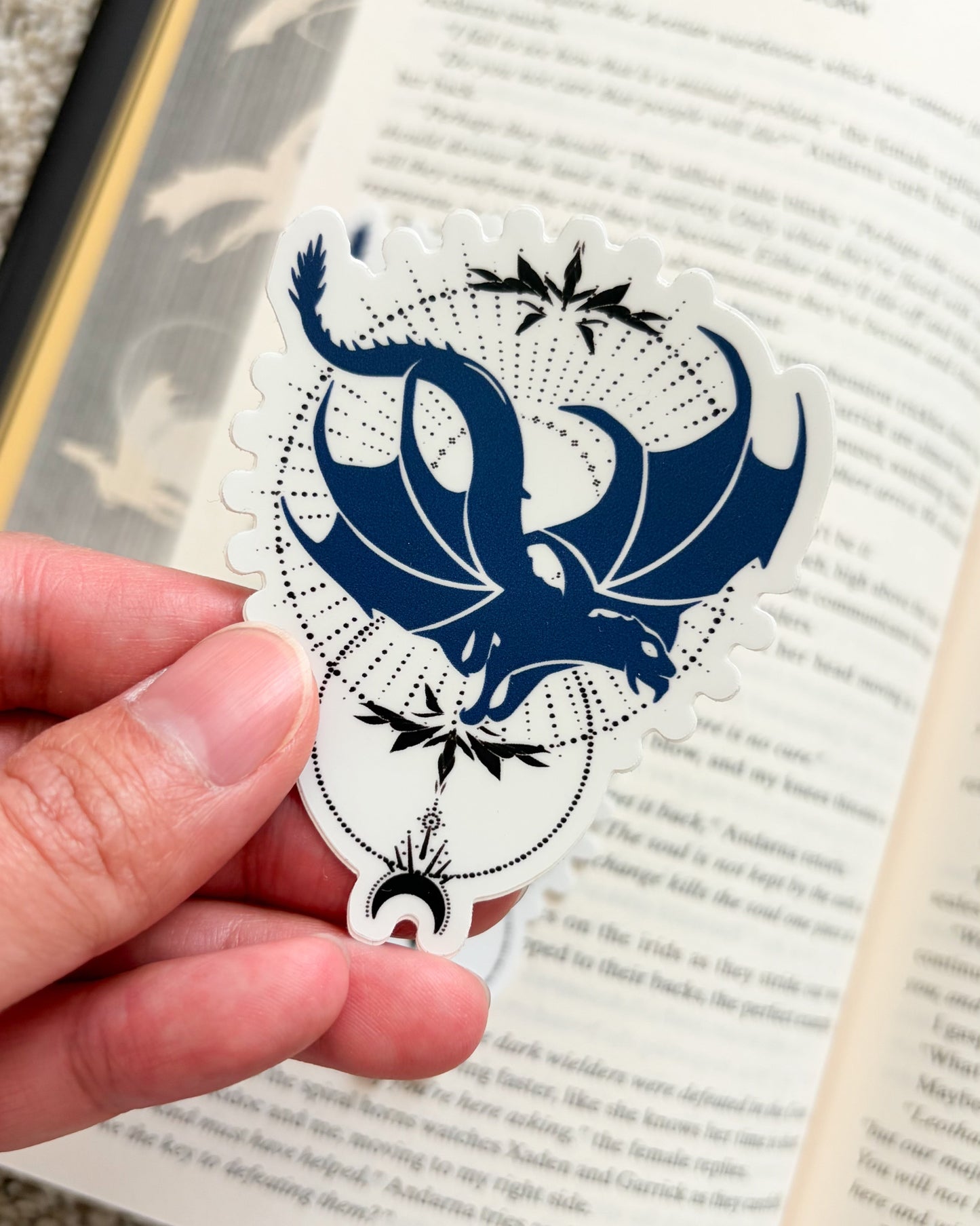 Hand holding a blue and white dragon-shaped bookmark over an open book.