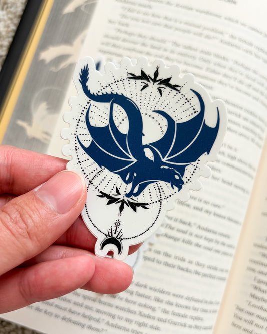 Hand holding a blue and white dragon-shaped bookmark over an open book.