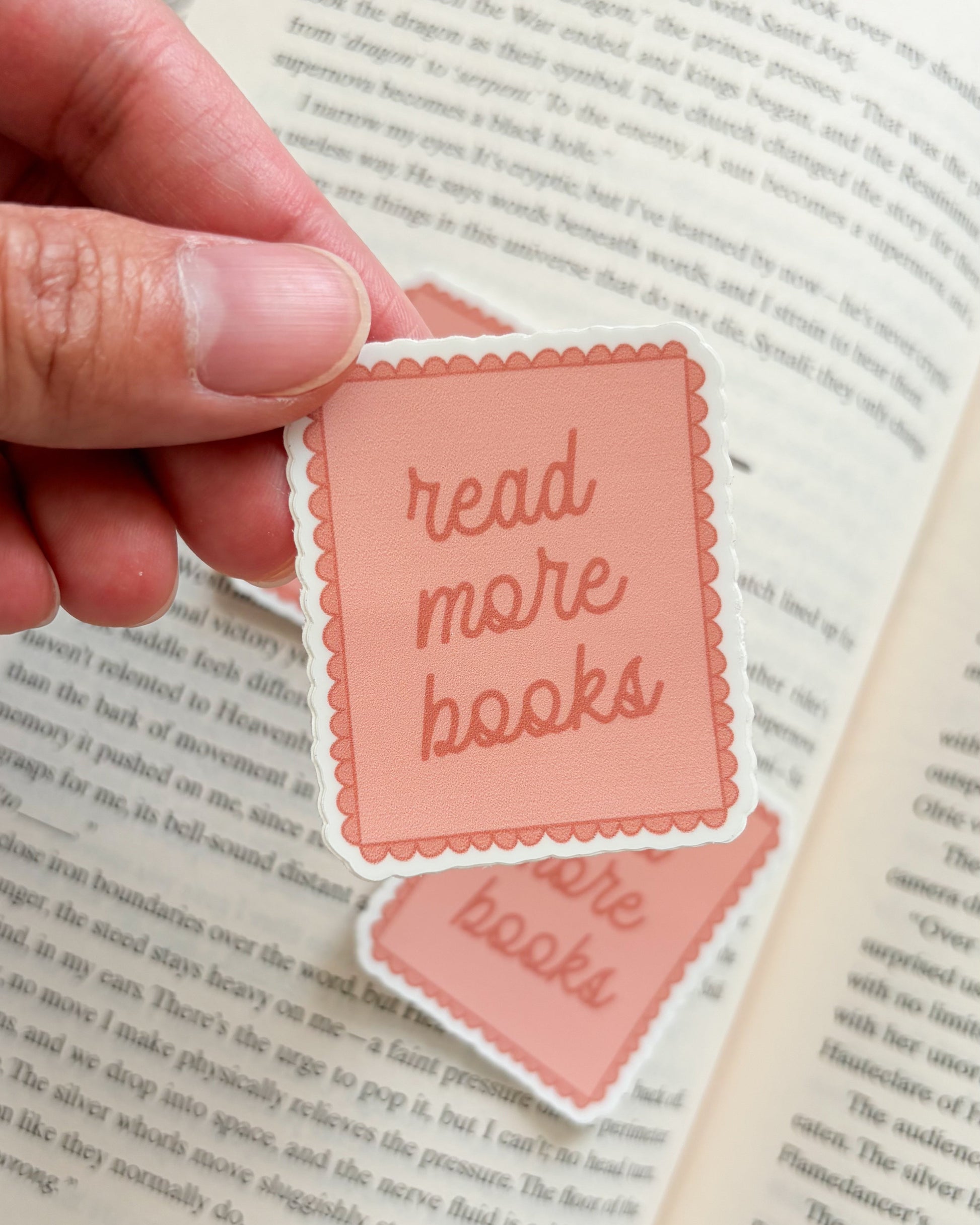 Hand holding a pink 'read more books' sticker over an open book